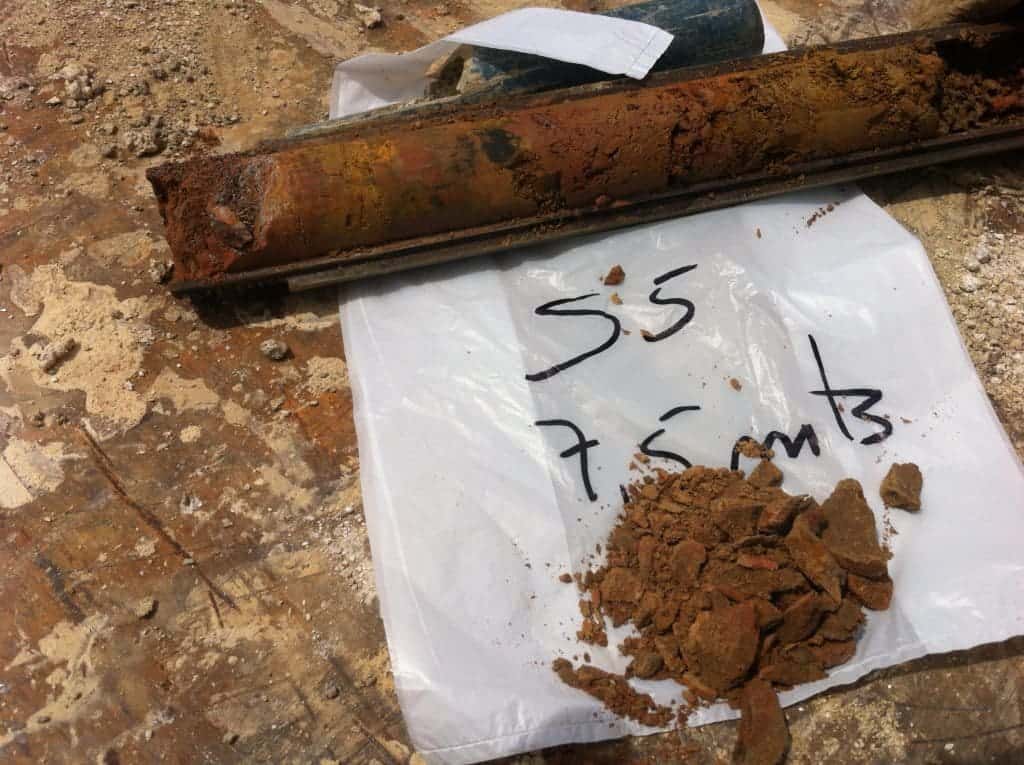 Sondagem hidrogeológica com tubo de aço e amostras de solo para análise de água subterrânea.
